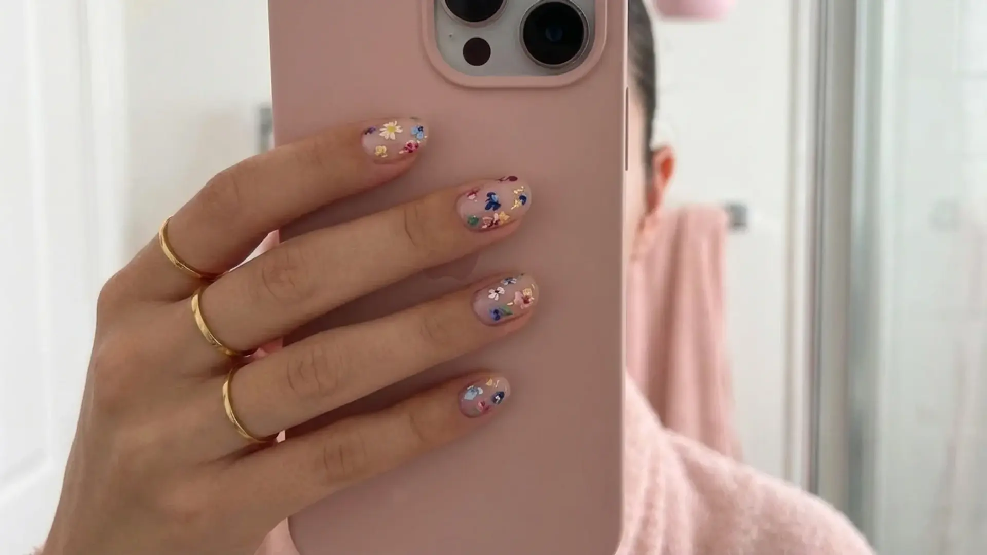 Mini floral nail design holding phone with gold rings showing soft pastel bridemaids nail ideas