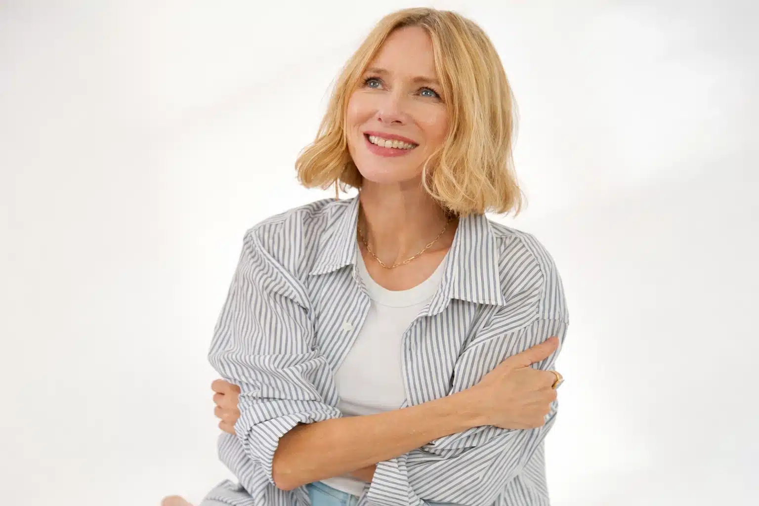 Naomi Watts with soft blonde hair wearing light striped shirt and neutral tones, reflecting light summer palette with airy styling