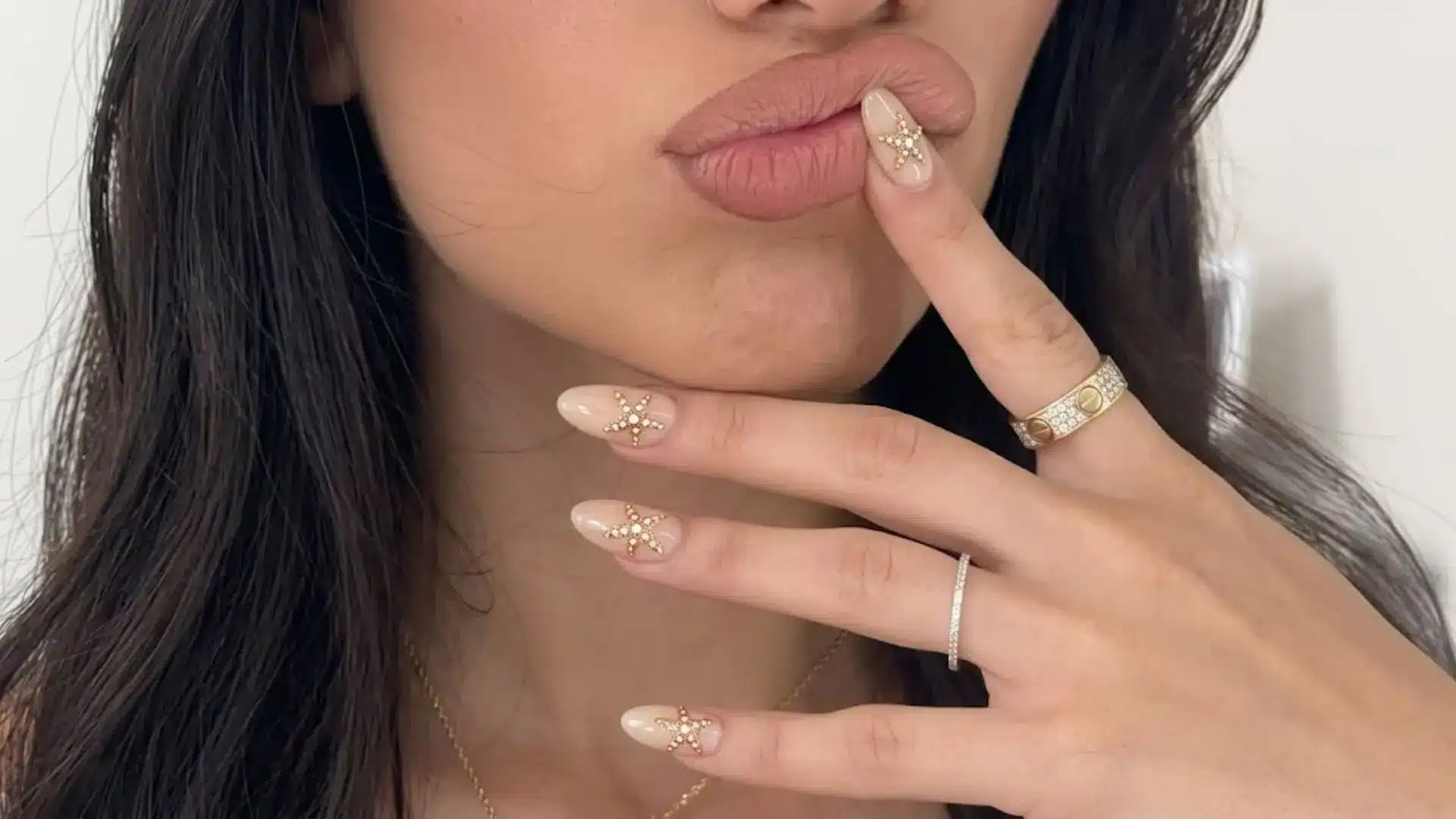 Nude almond nails with gold starfish accents near lips, minimalist beach manicure with elegant jewelry styling
