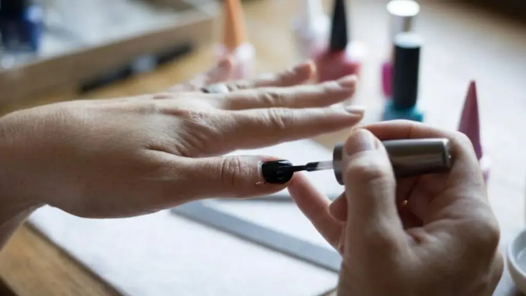Person applying black nail polish carefully on fingernails at home with manicure tools placed on table nearby