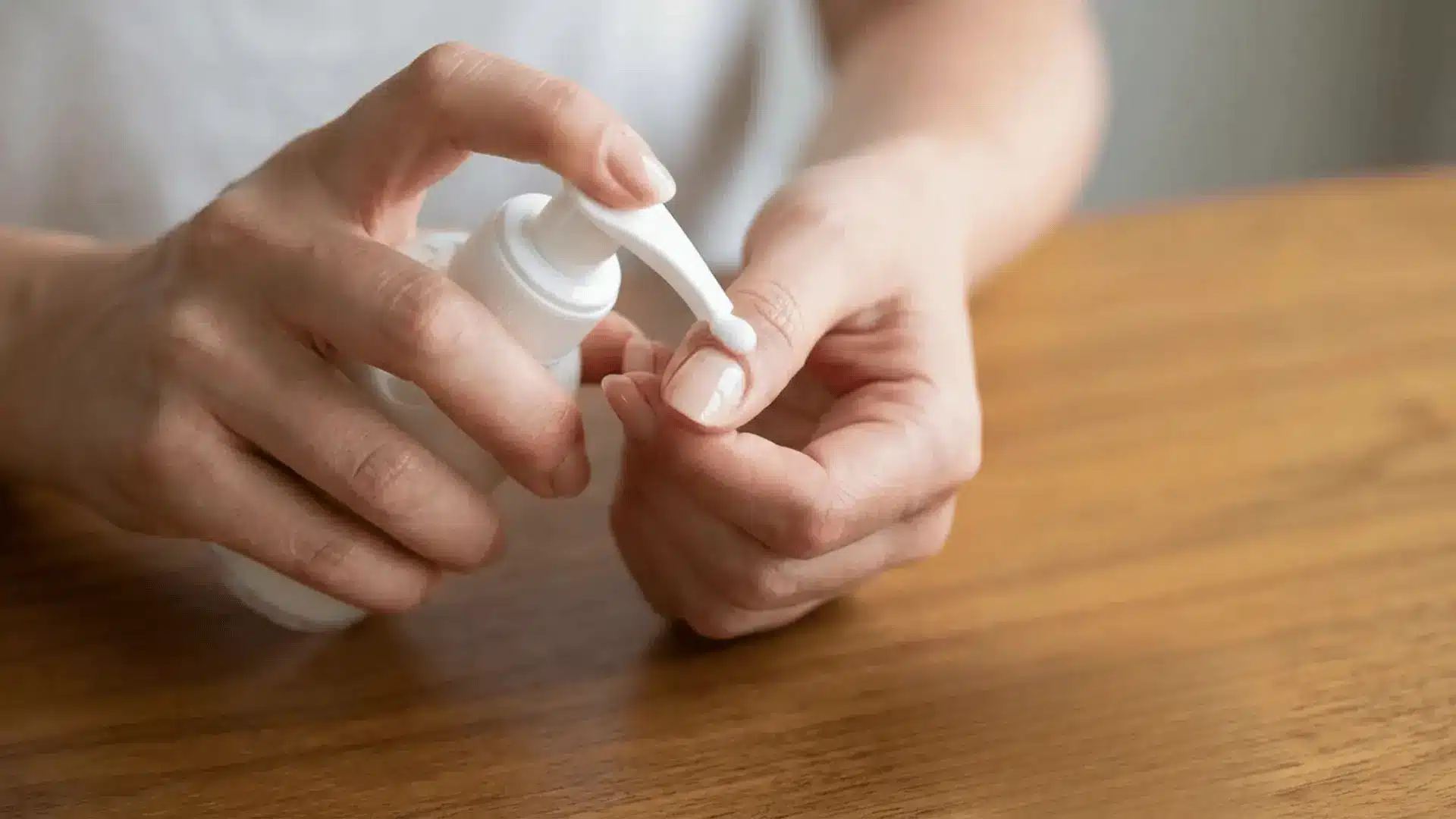 Person applying lotion to fingers to help loosen nail glue stuck on skin after press on nails