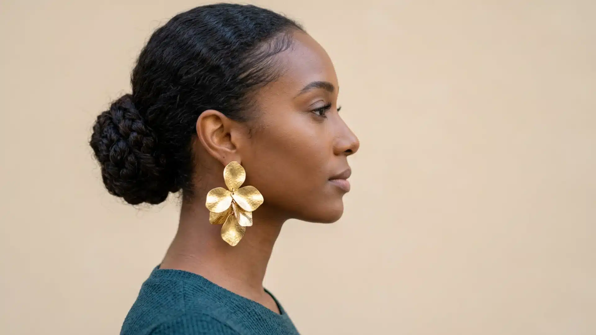 Profile of a Black woman with hair in a braided bun, wearing large, statement gold flower petal earrings