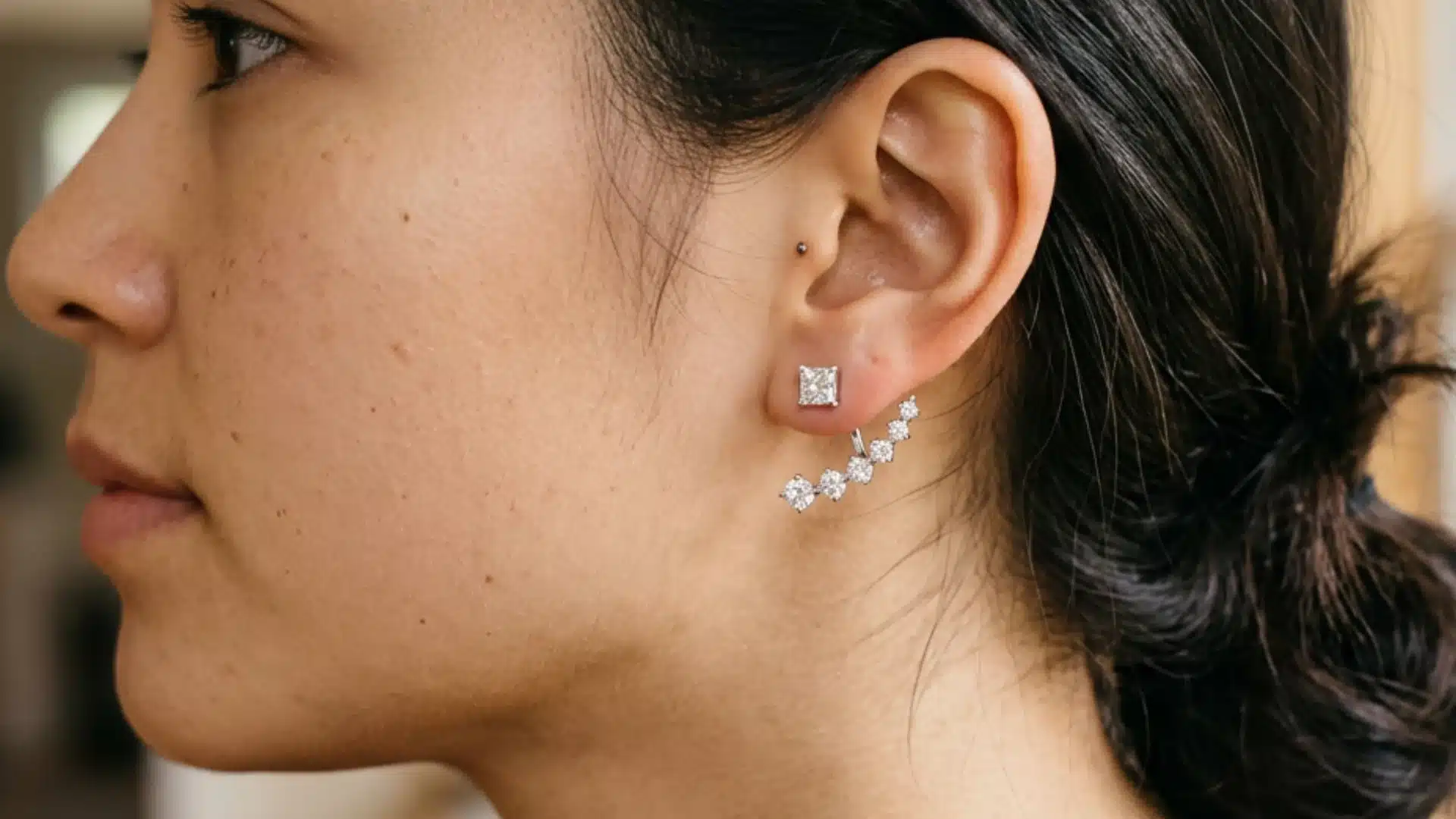 Profile of a woman with dark hair in a bun, wearing a square stud earring with a curved diamond ear jacket jacket