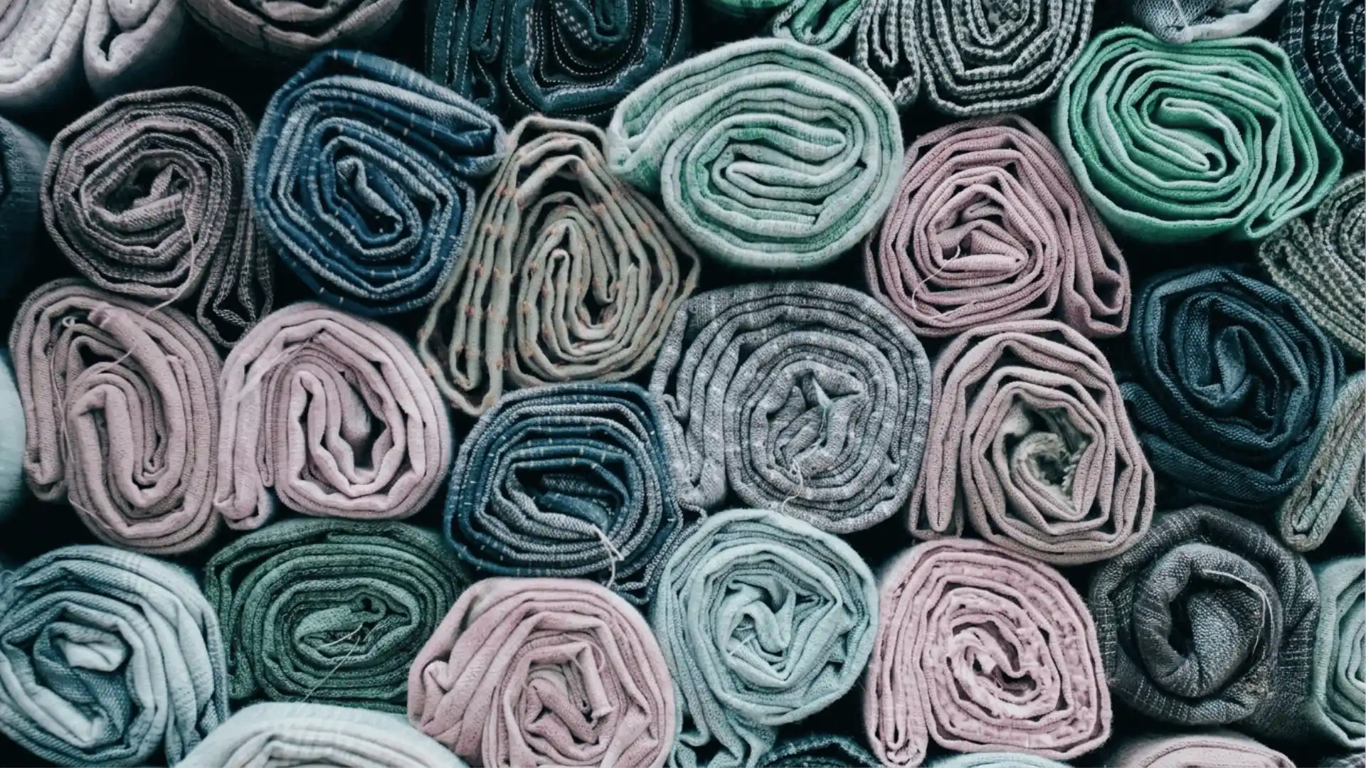 Rolled modal fabric in soft pastel and dark tones arranged closely to show texture and color variety