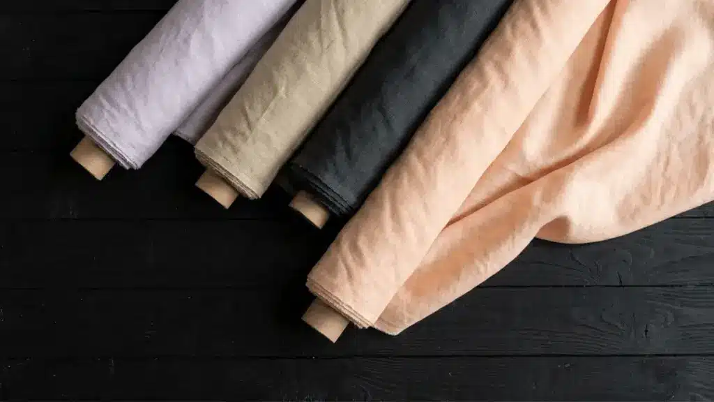 Rolls of neutral colored modal fabric on a dark wooden surface, showing soft texture and natural folds