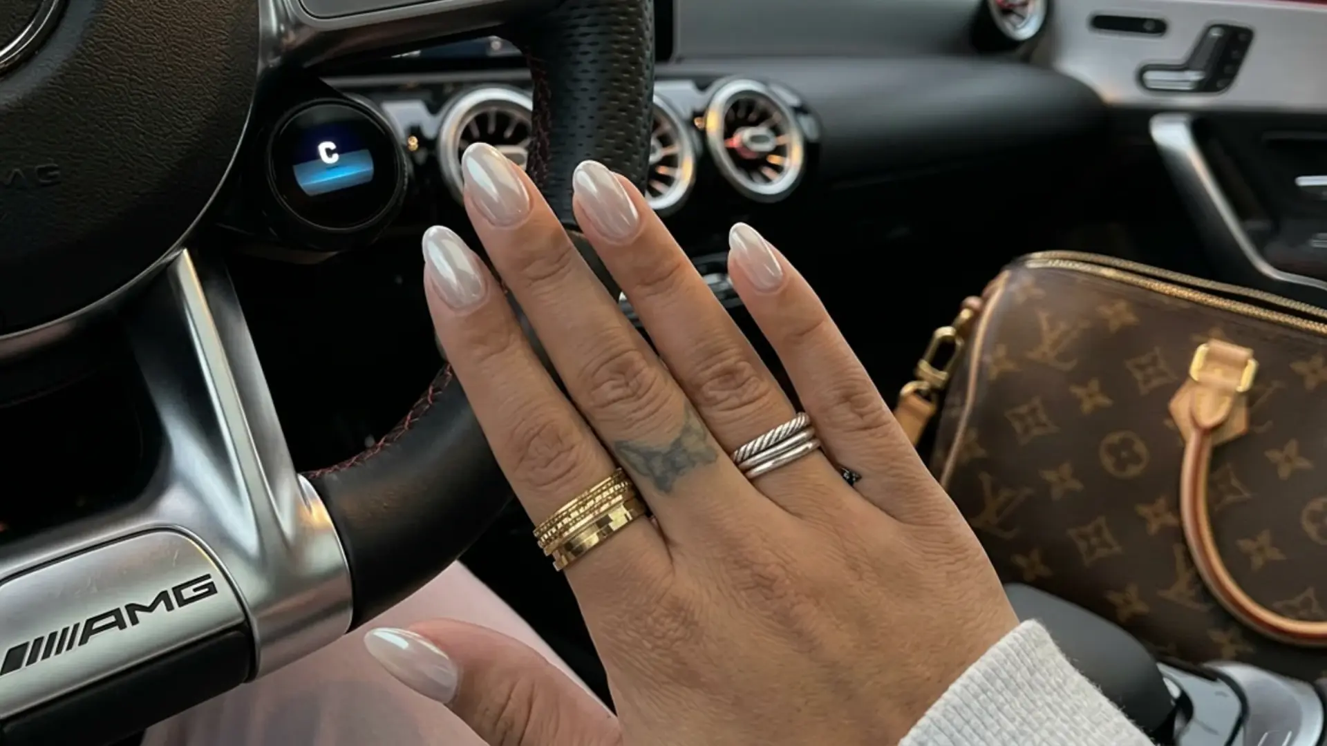 Sheer Milky Chrome almond manicure with stacked rings on steering wheel showing classy bridemaid nail ideas