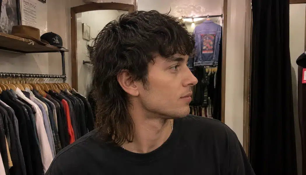 Side profile of a young man with a modern shaggy mullet in a vintage clothing store