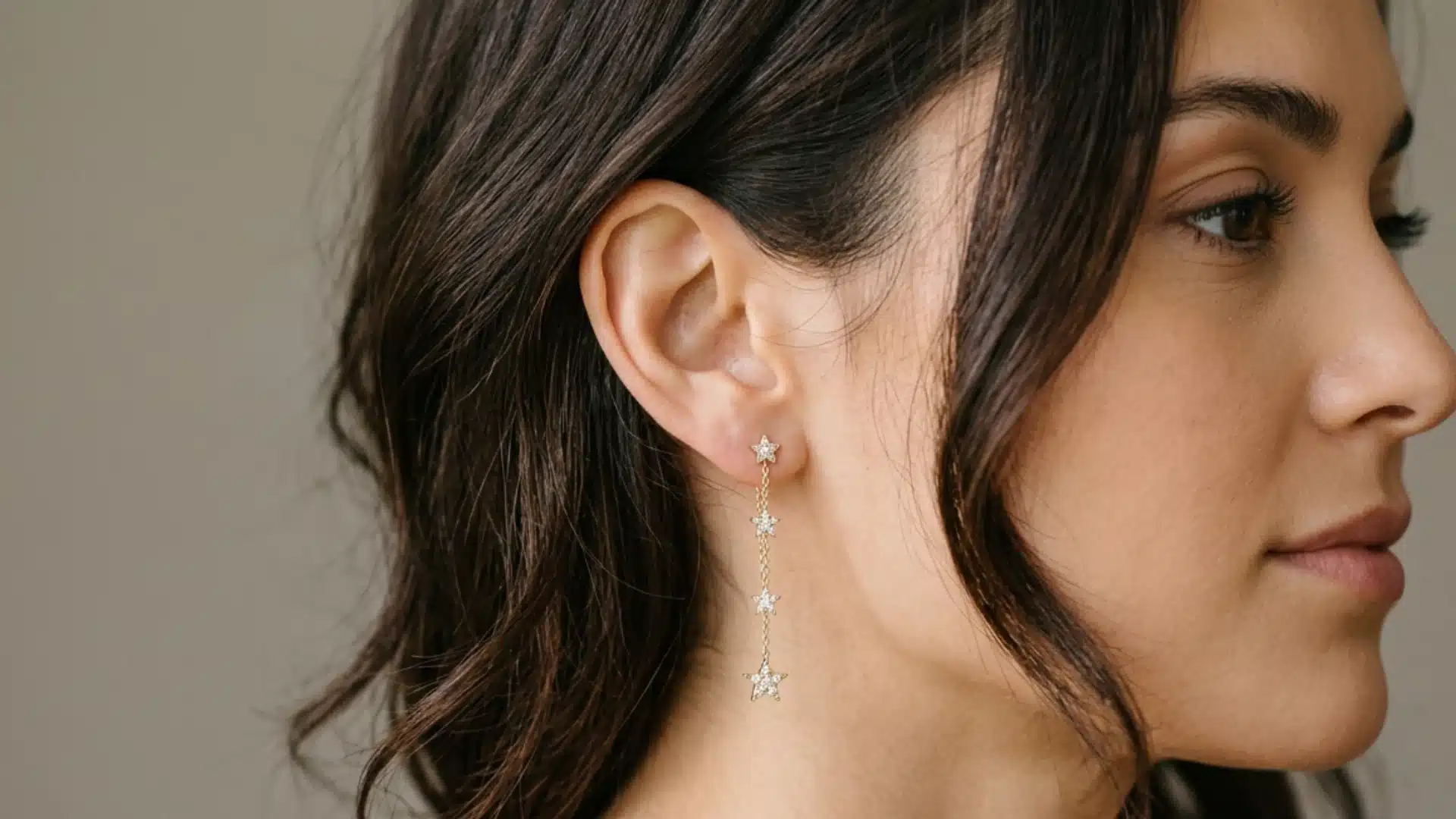 Side profile of a woman with dark wavy hair, wearing a gold drop earring with a vertical chain of four stars
