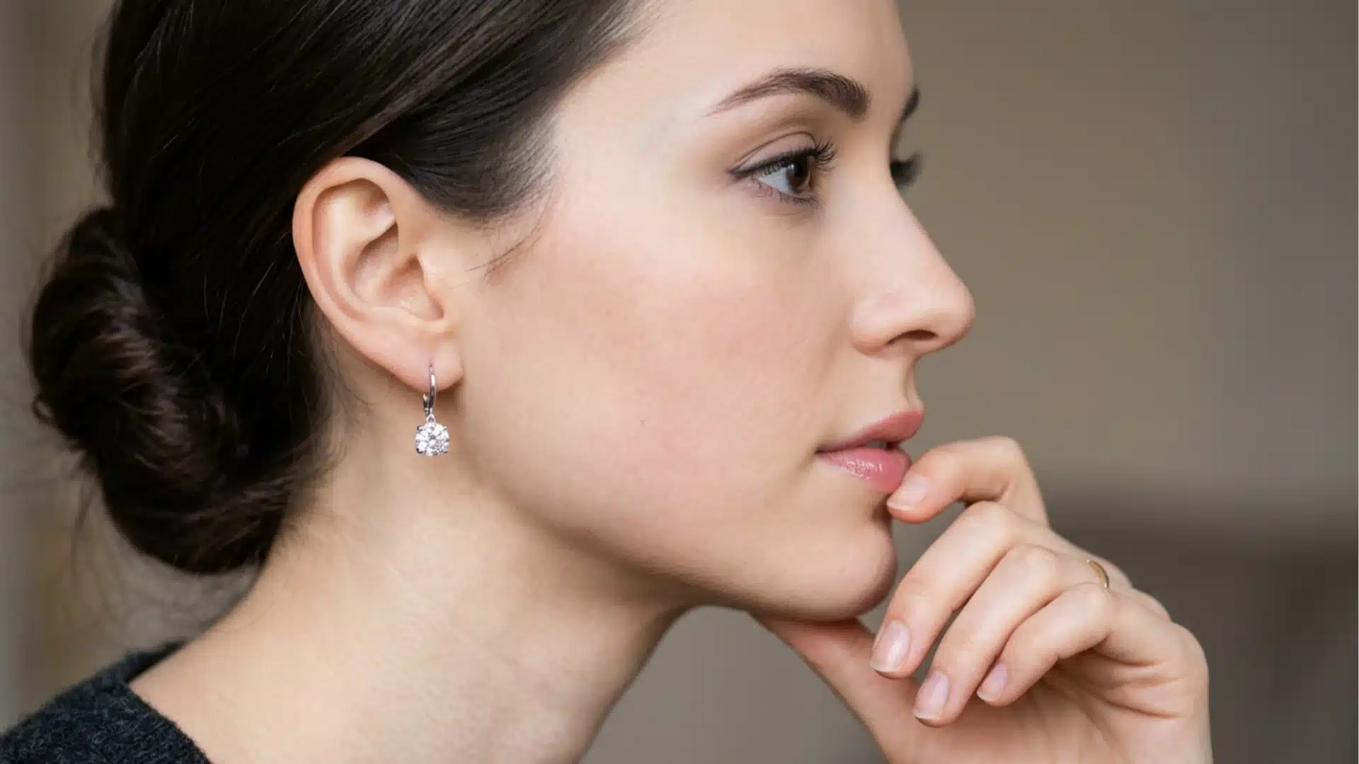 Side profile of a woman with her hair in a bun, wearing a silver drop earring with a round diamond