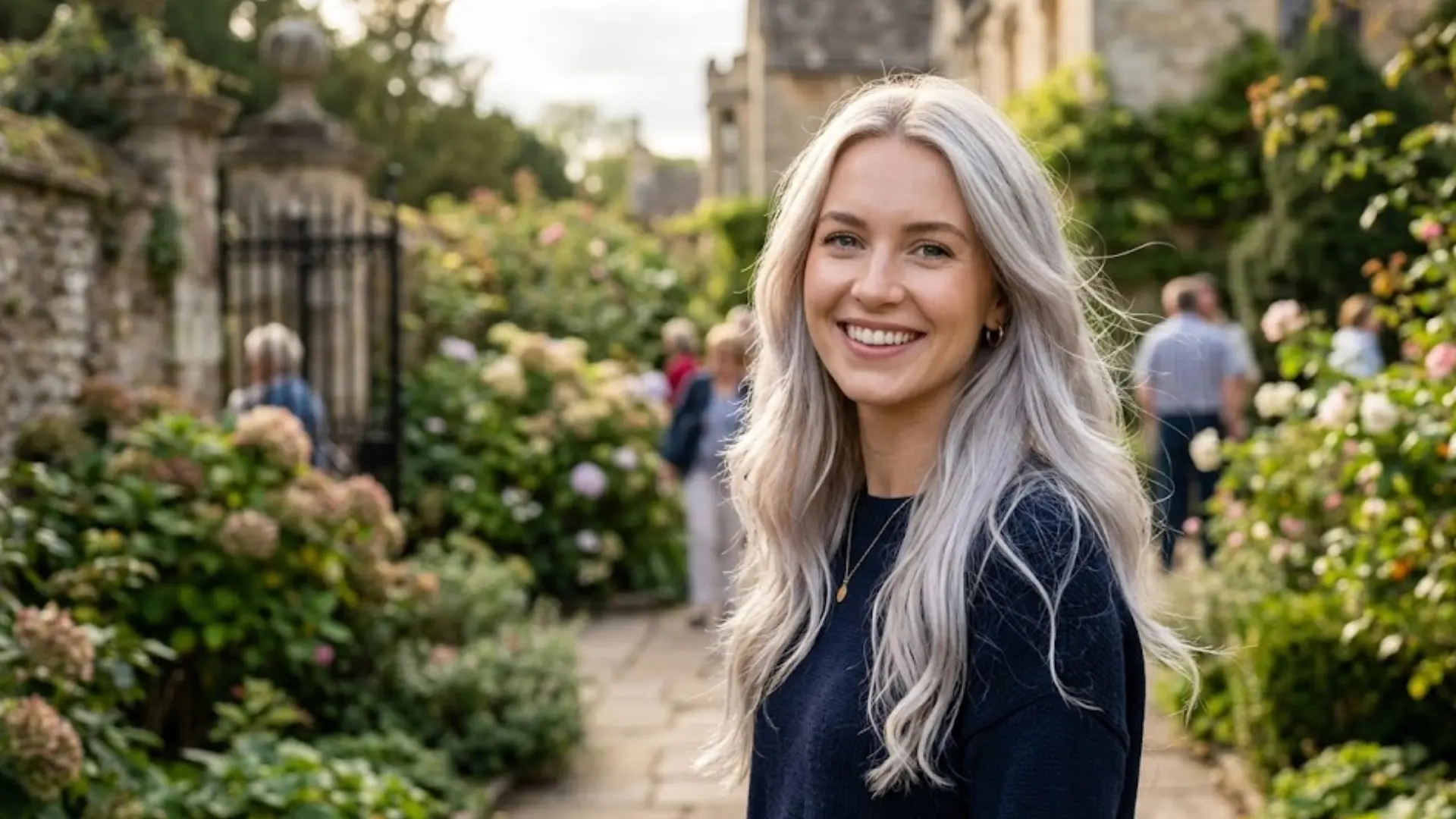 Smiling woman with cool toned silver blonde hair standing in garden, showcasing soft icy shade and healthy long hair texture