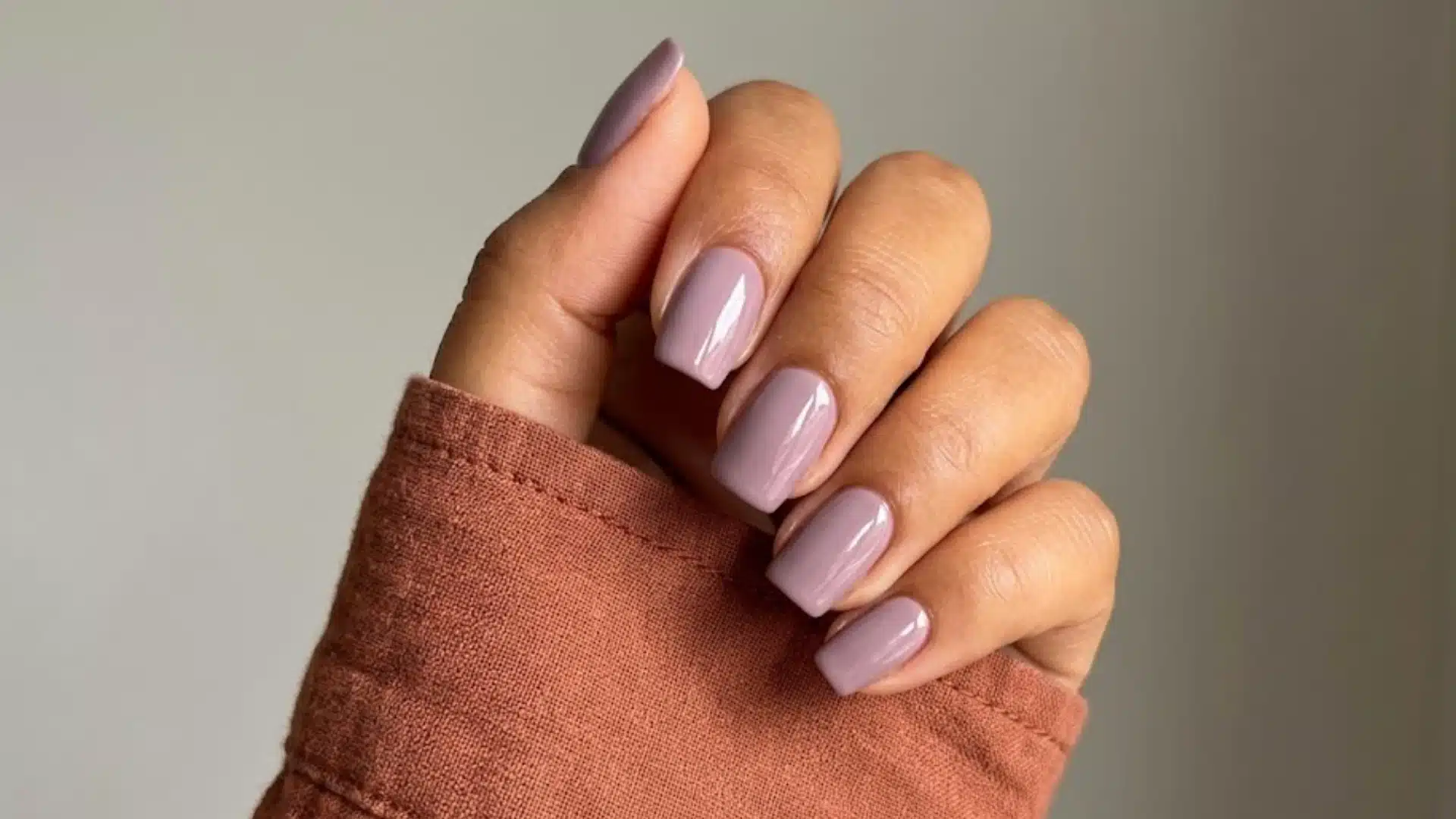 Soft mauve glossy nails on short square tips, minimal look with cozy sleeve detail and neutral background