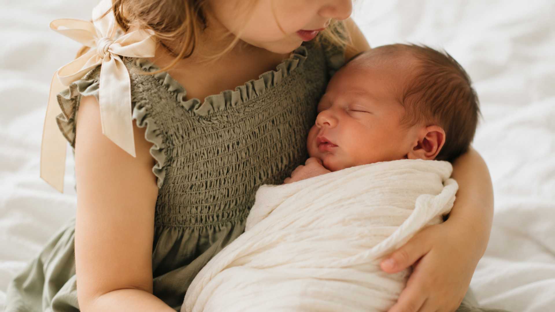 Toddler in sage green smocked dress holding swaddled newborn in family photography session