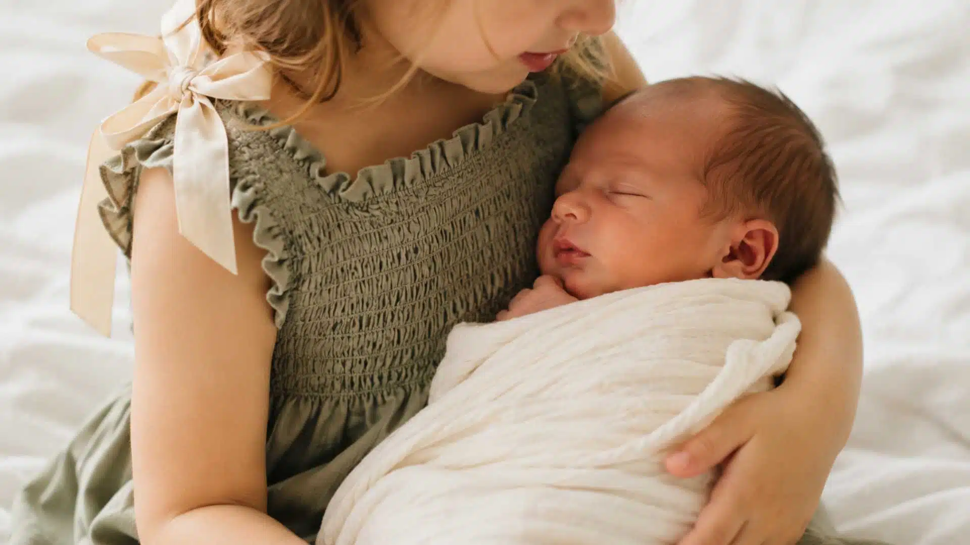 Toddler in sage green smocked dress holding swaddled newborn in family photography session
