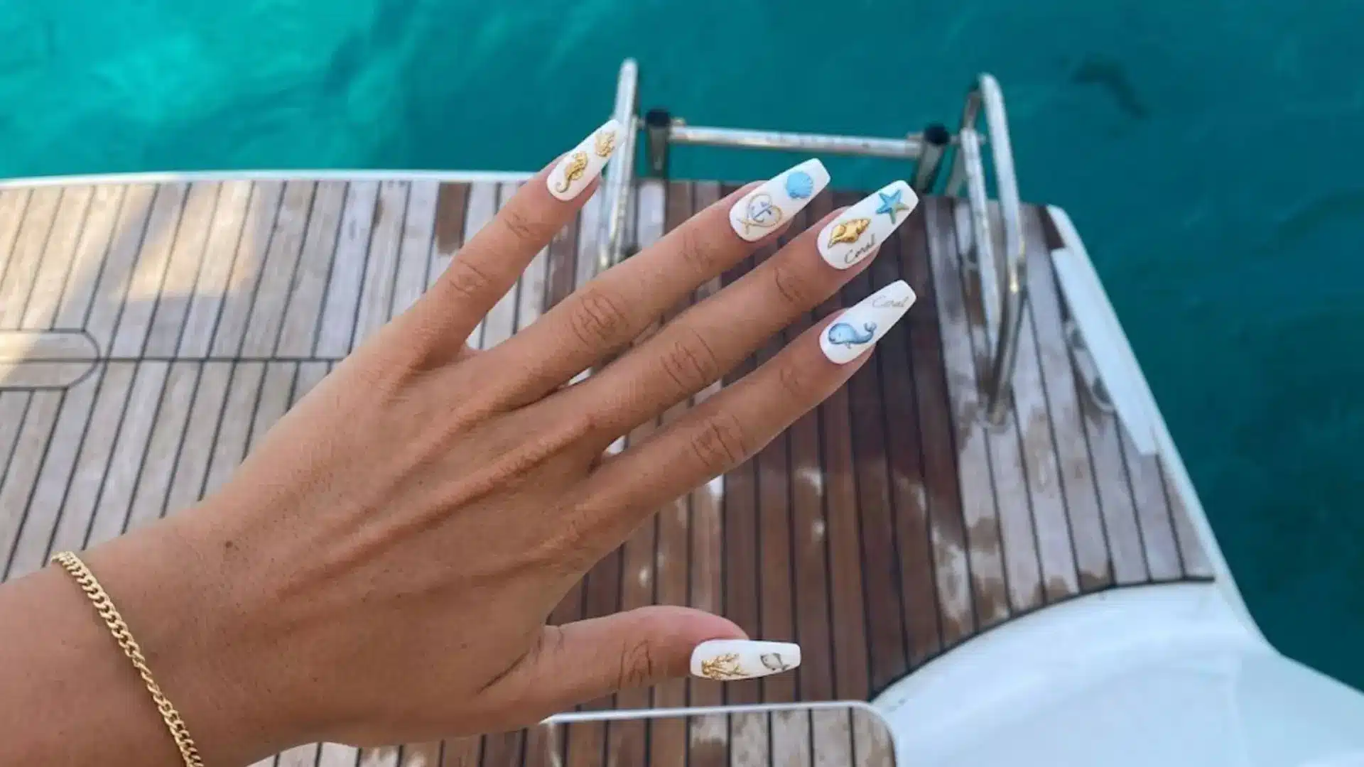 White square nails with seashell, starfish, and coral art over ocean deck, tropical beach nail design ideas