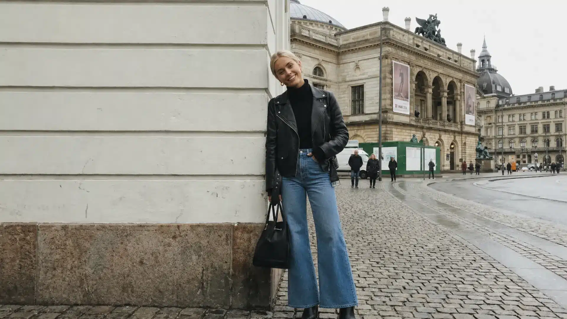 Woman in a cropped leather jacket and flare jeans posing on a European cobblestone street