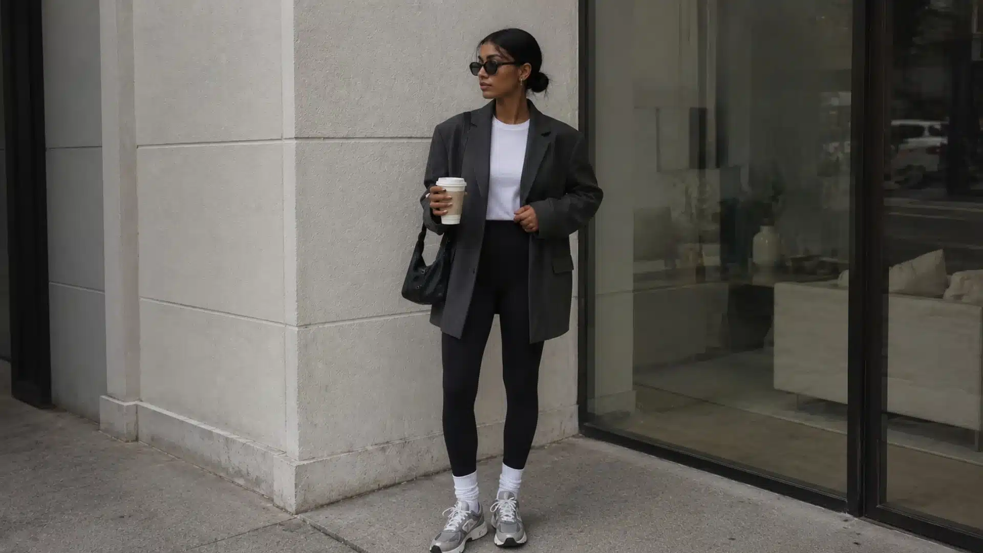 Woman in oversized blazer and black leggings standing outside a modern city storefront