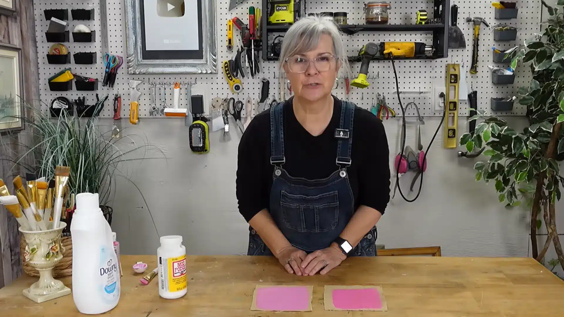 Woman standing behind wooden table displaying two pink painted fabric squares left to dry