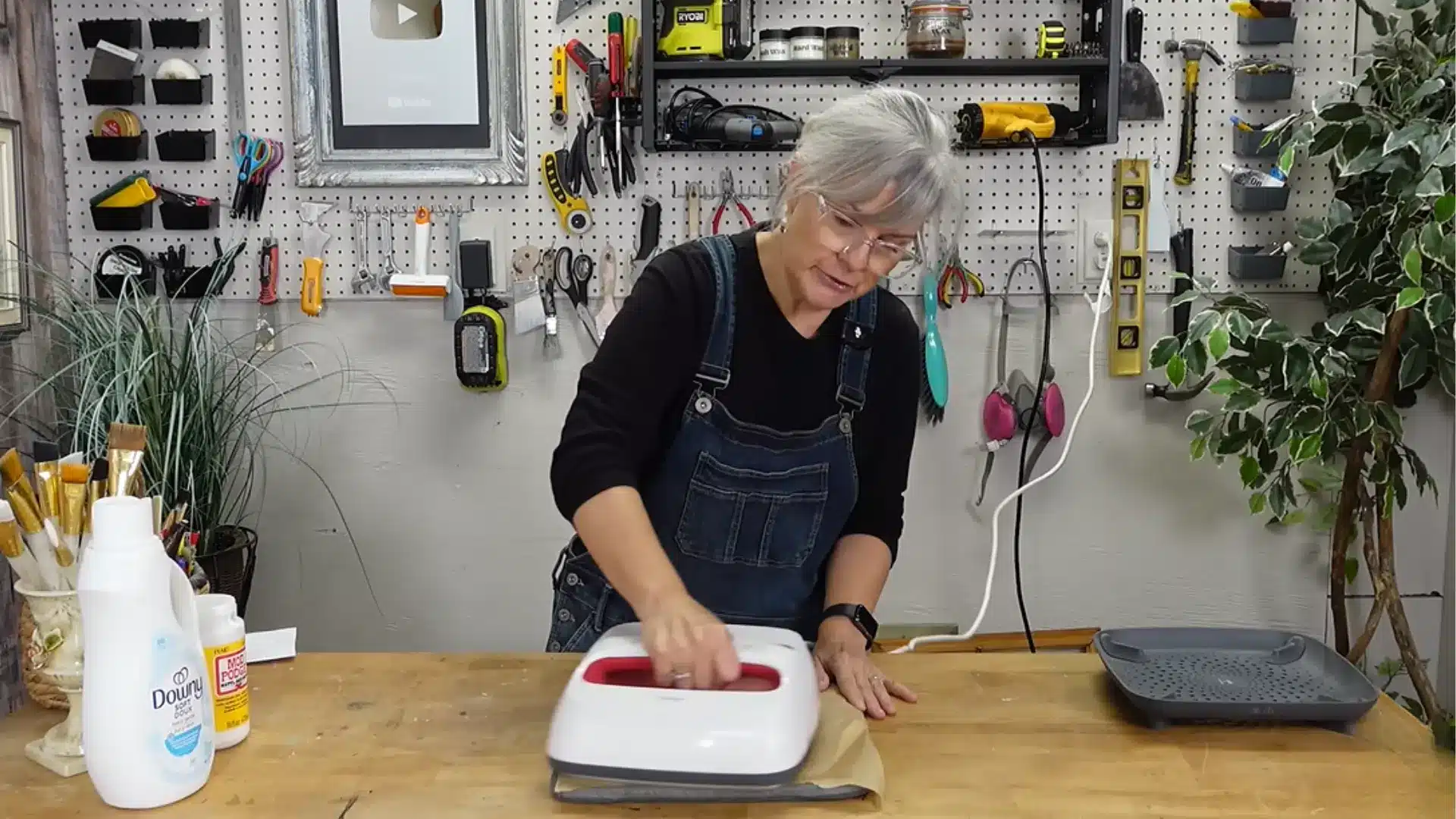 Woman using a white heat press machine to heat set pink painted fabric on a wooden table