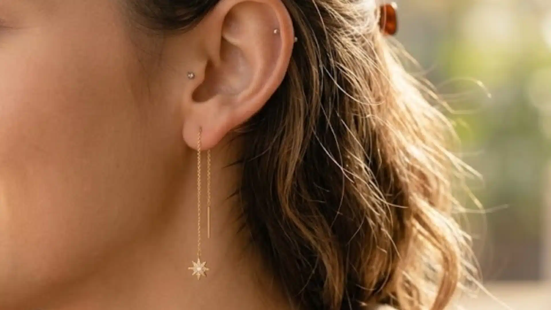 Woman wearing delicate gold threader earrings with a star charm while holding coffee in soft daylight