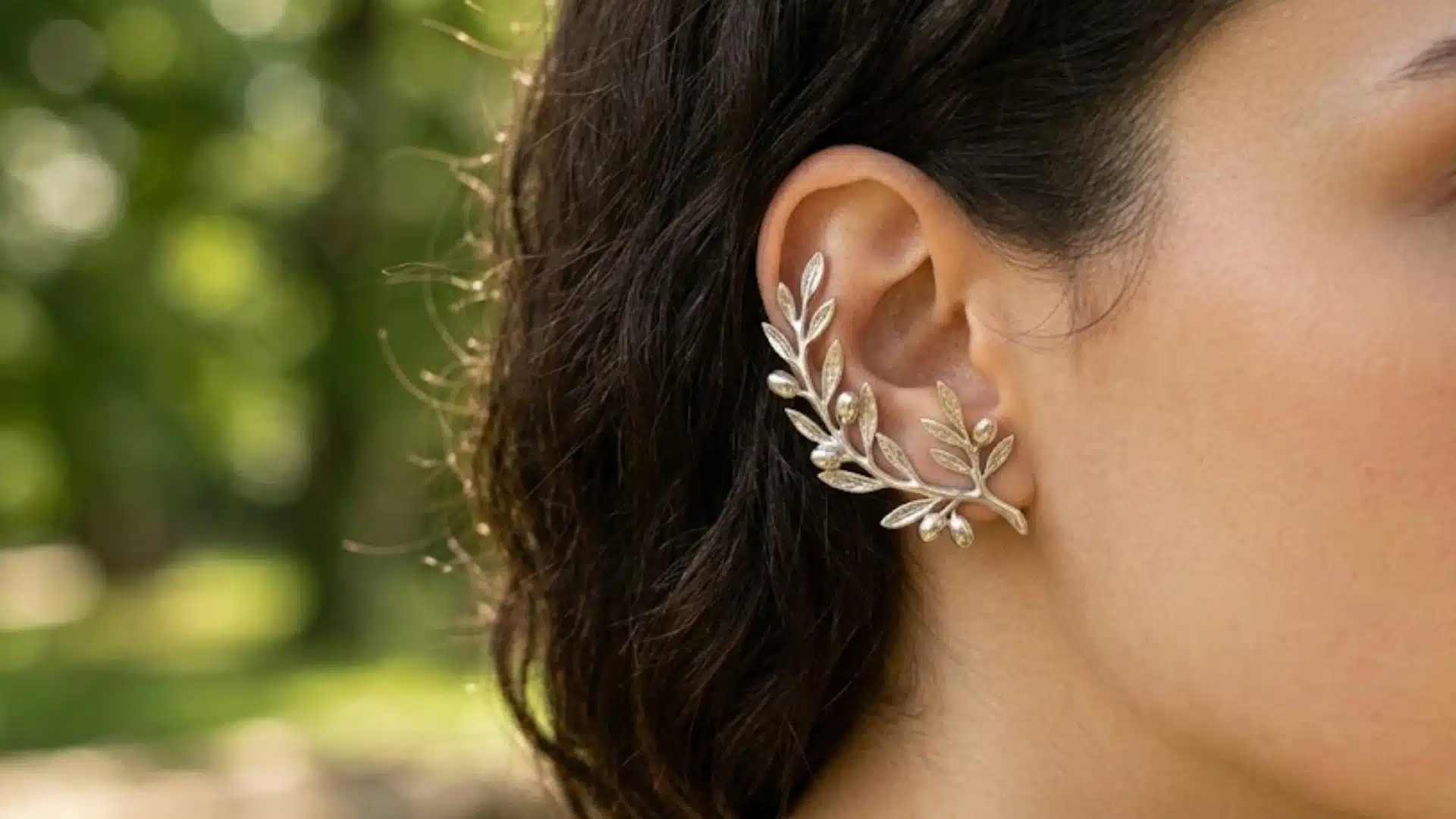 Woman wearing silver leaf ear climber earrings that curve upward along the ear in a green outdoor setting