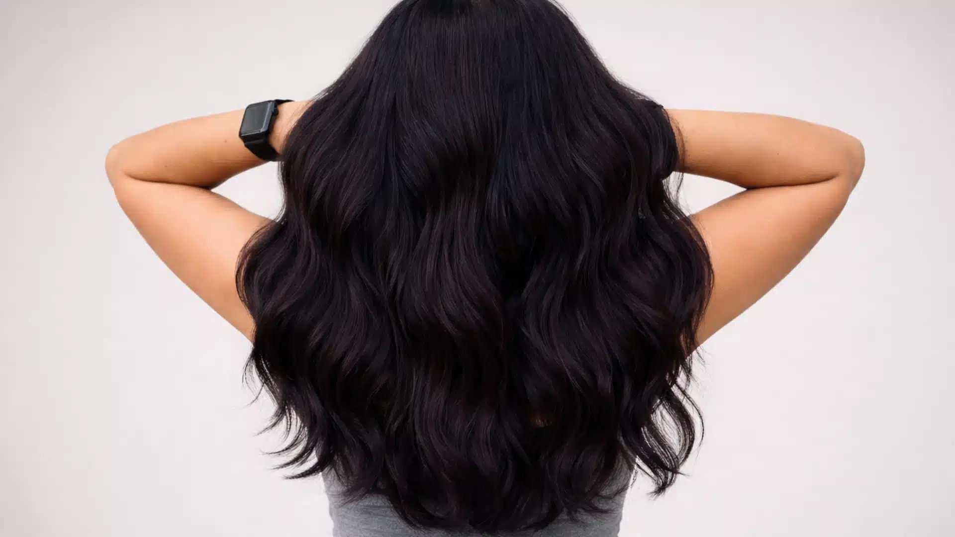 Woman with long cool-toned dark wavy hair against a solid neutral background, showing smooth texture and shine