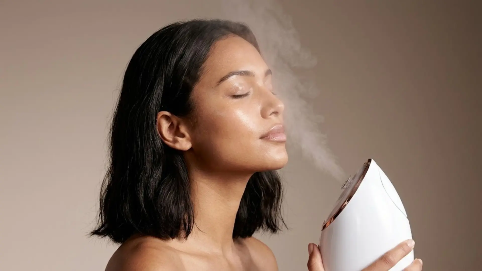 Woman using a facial steamer as warm mist reaches her face
