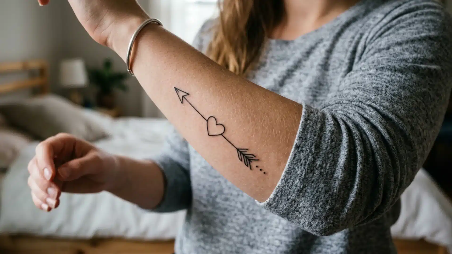 A fine-line arrow tattoo with a heart in the middle on a woman's outer forearm, pointing toward her wrist
