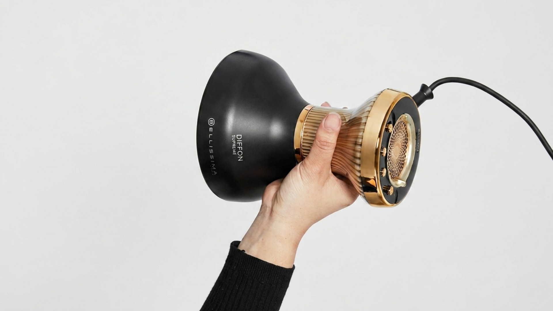 A hand holding a black and gold Bellissima Diffon Supreme hair diffuser against a plain white background
