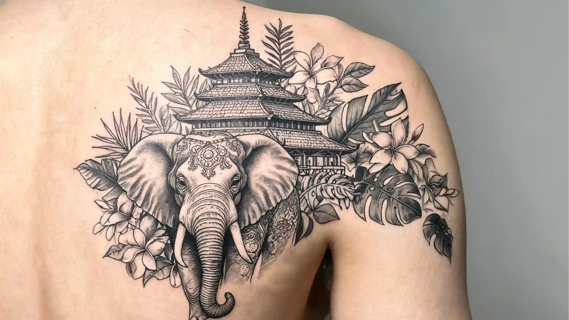 Asian elephant tattoo with temple pagoda, tropical flowers, and leafy details on upper back