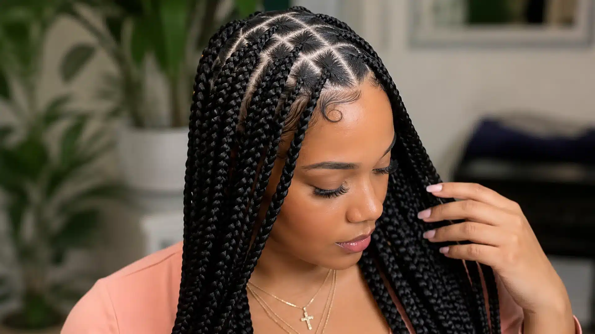 A woman looking down, showcasing neat diamond-parted knotless box braids with a sleek, curled hairline edge