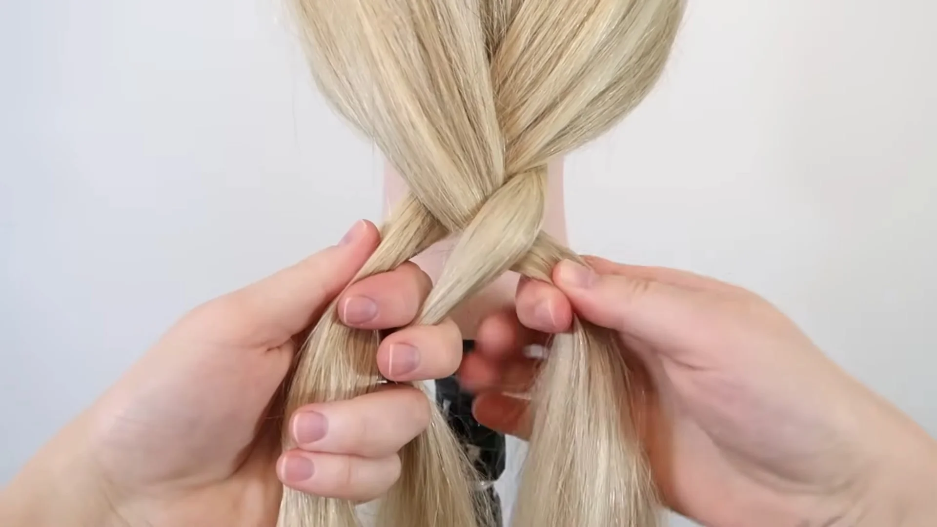 Blonde hair strands being crossed over the center section during a three-strand braid, demonstrating the basic braiding technique step by step.