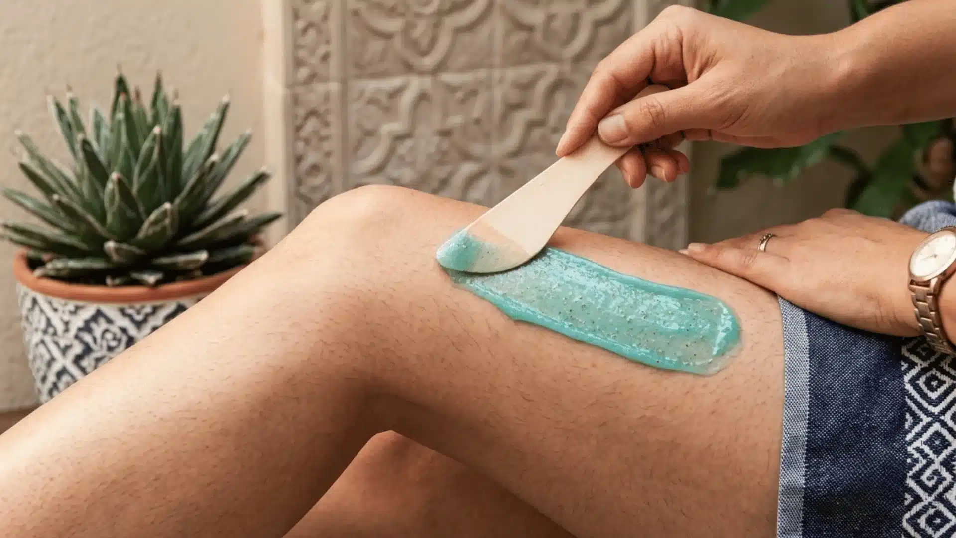 Blue wax being applied to a hairy leg with a wooden spatula during a waxing treatment