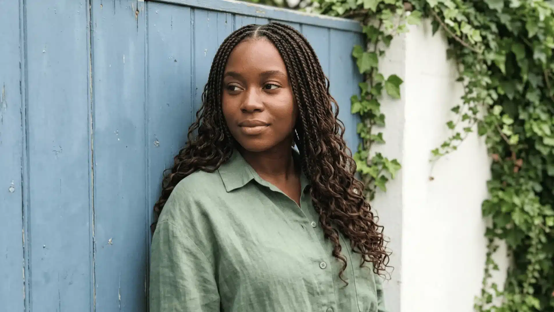 _Boho knotless braids in dark brown with flat scalp roots and soft loose curly ends on a medium brown-skinned woman against a garden wall