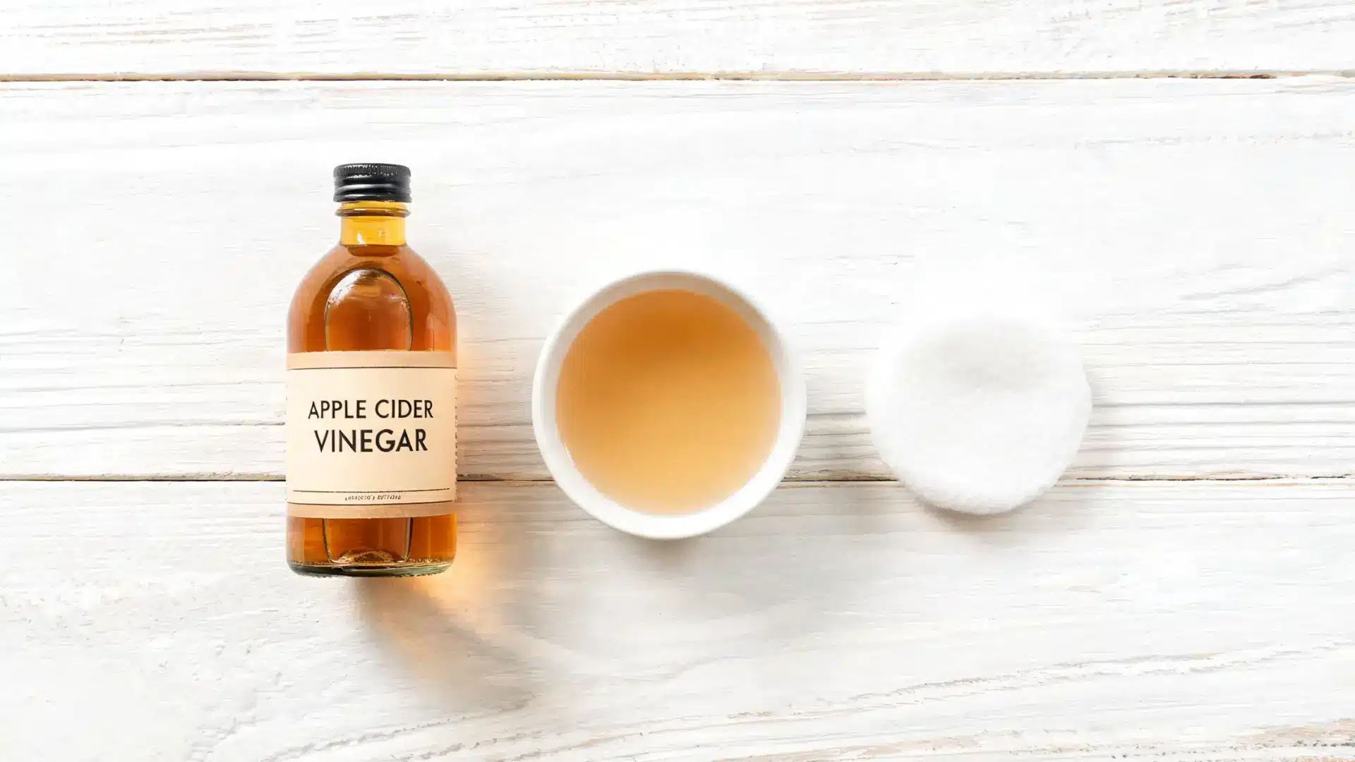 Bottle and bowl of apple cider vinegar with a cotton pad.