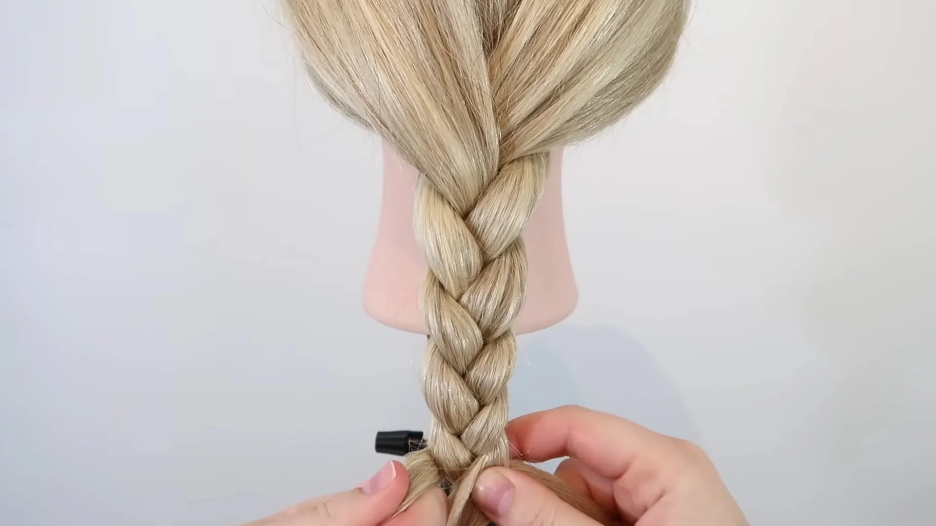 Completed three-strand braid on long blonde hair, showing the neat woven pattern formed after repeating the braiding technique to the end.