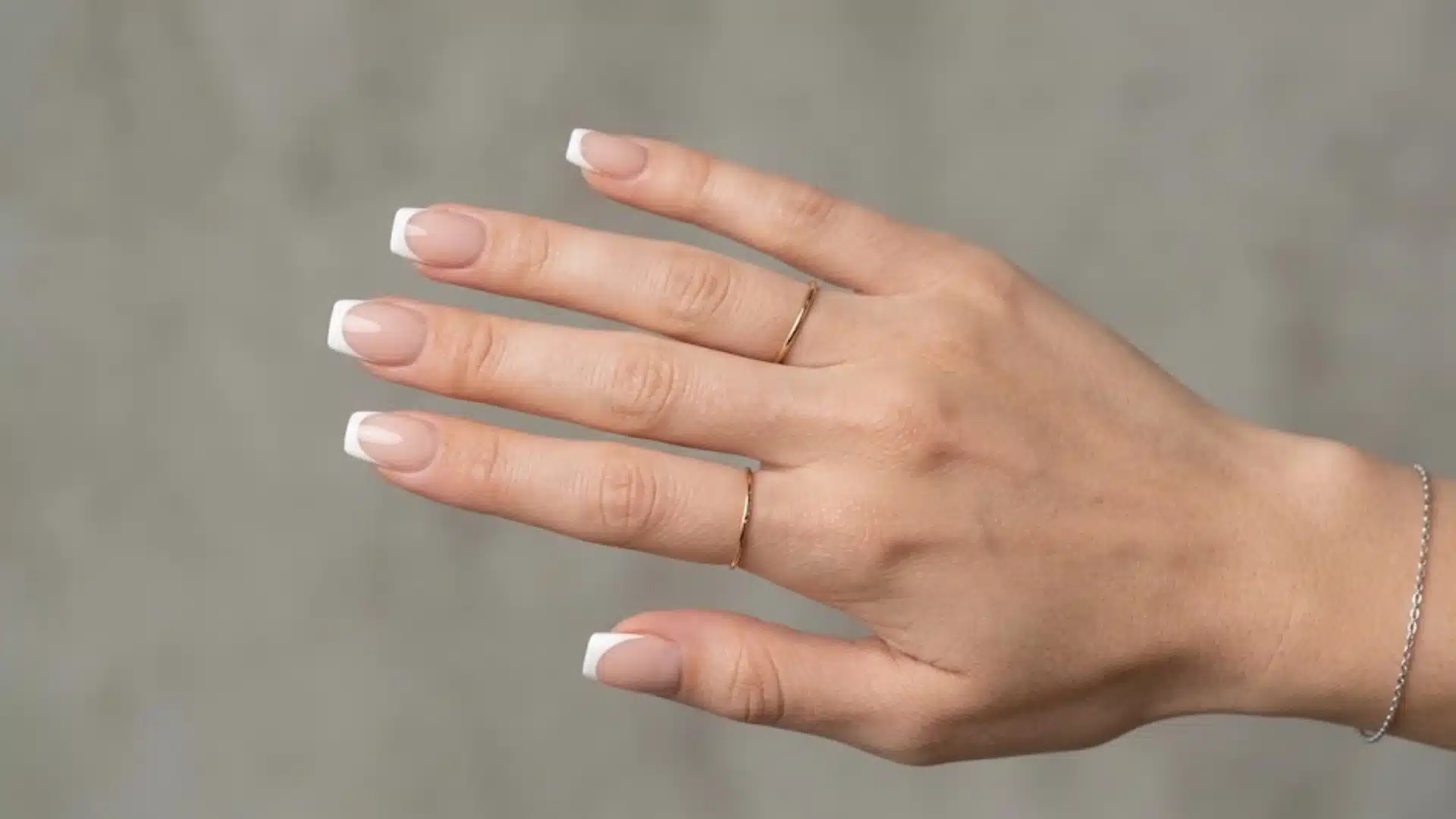 French manicure on square nails with nude base, white tips, gold rings, and delicate bracelet on hand