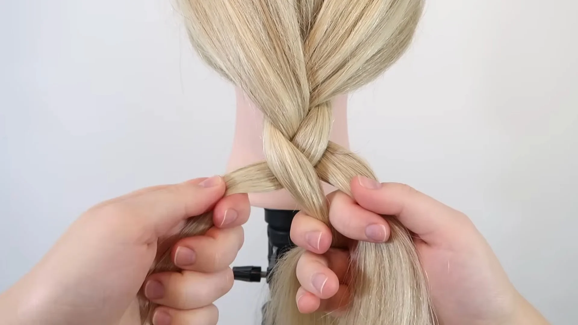 Hands alternating the outer hair sections over the middle strand, continuing a classic three-strand braid on long blonde hair.