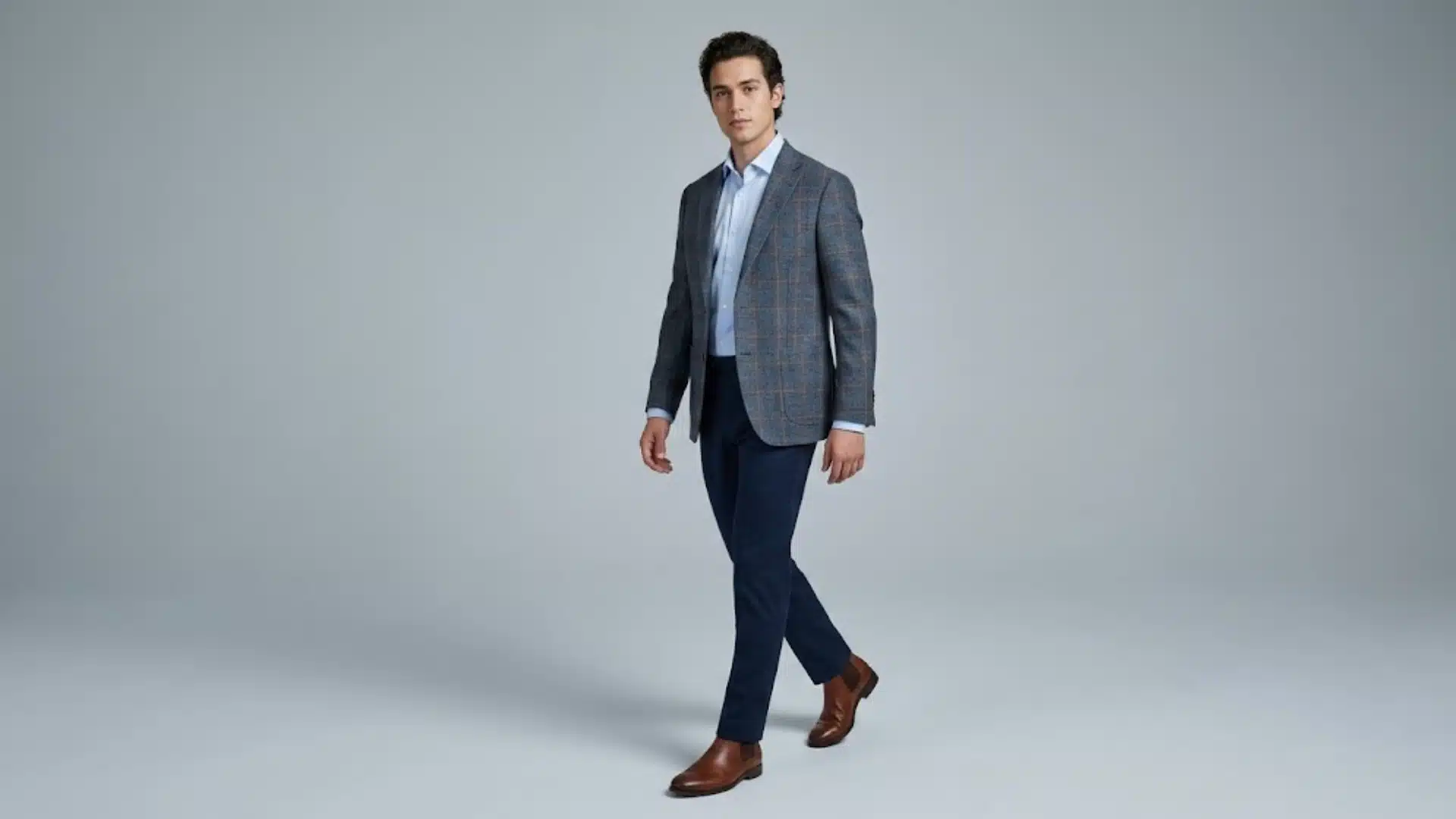 Man wearing a grey checked sport coat with navy trousers and brown dress boots