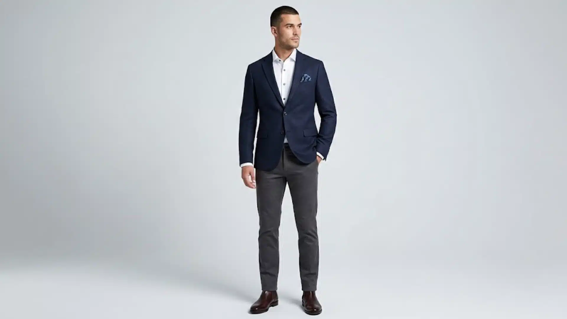 Man wearing a navy blazer with grey trousers, white shirt, pocket square, and brown dress shoes
