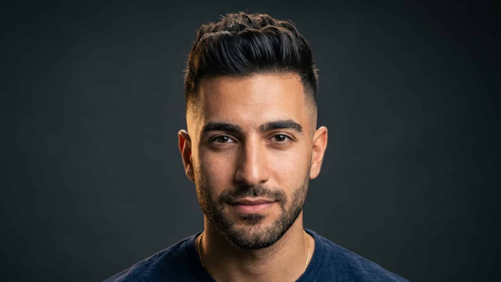 Man with a styled short quiff haircut and a beard looking forward against a dark background