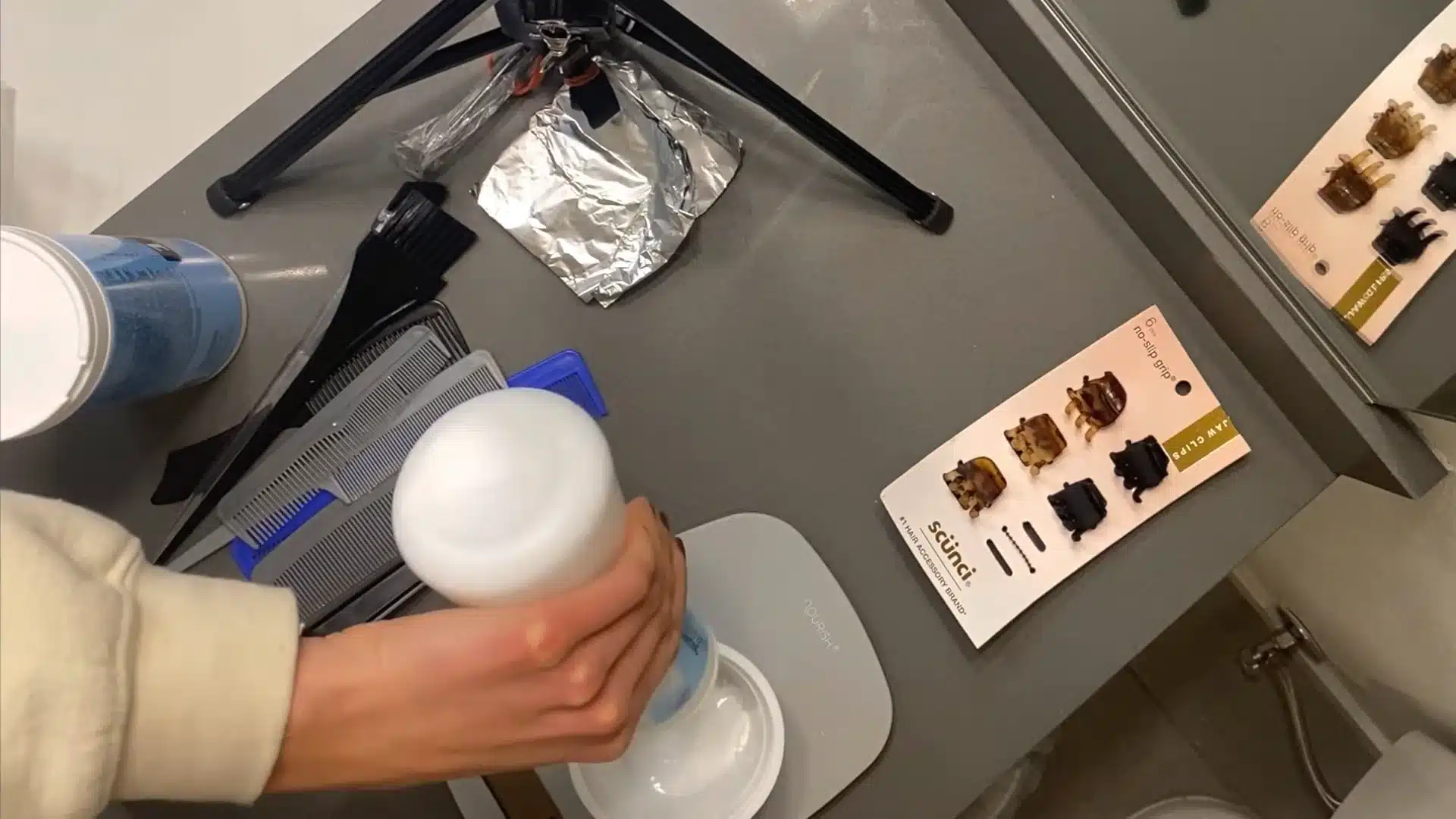 Mixing hair bleach and developer in a bowl with foils and clips on bathroom counter