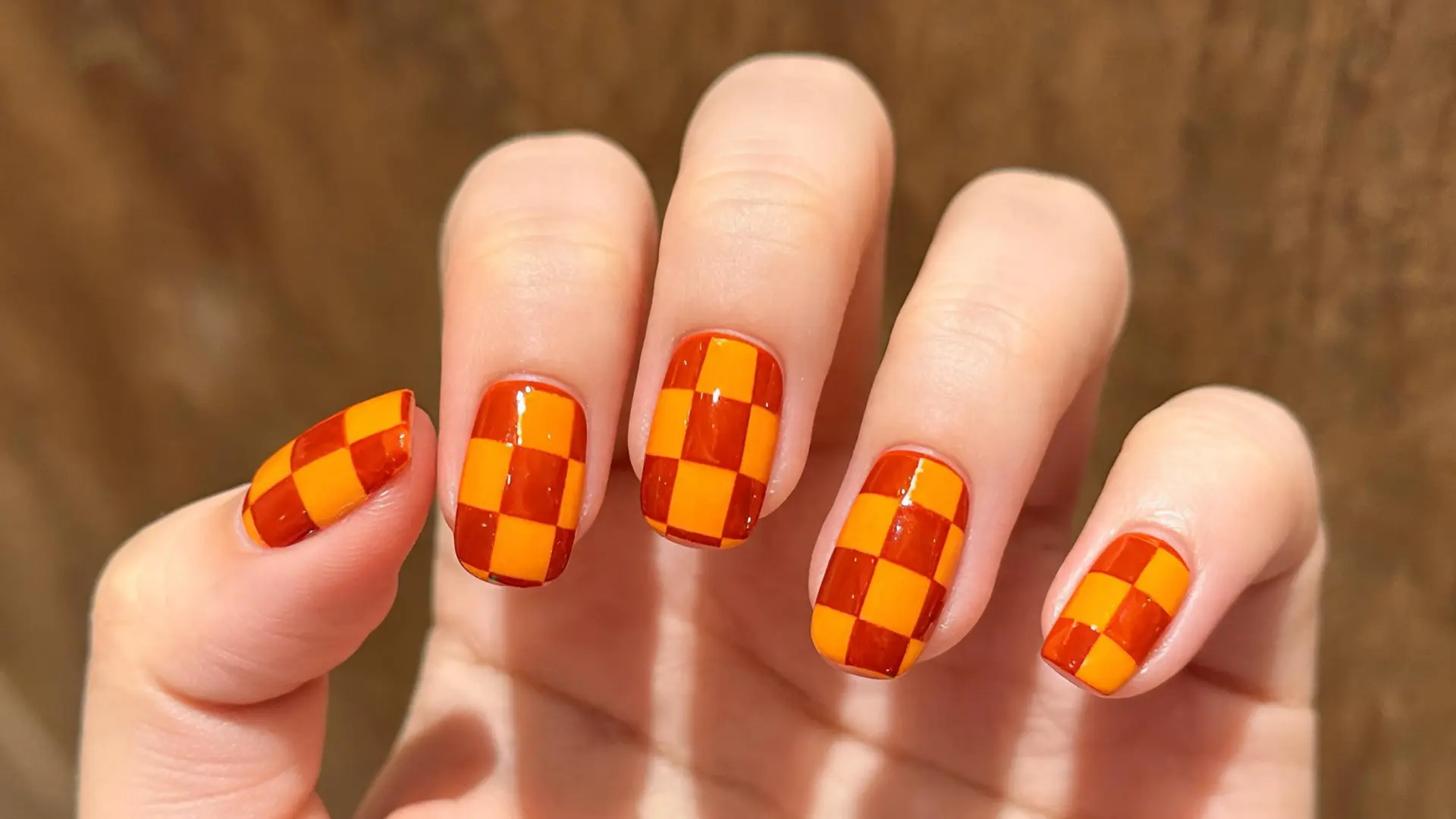Orange checkerboard nail design on short glossy nails