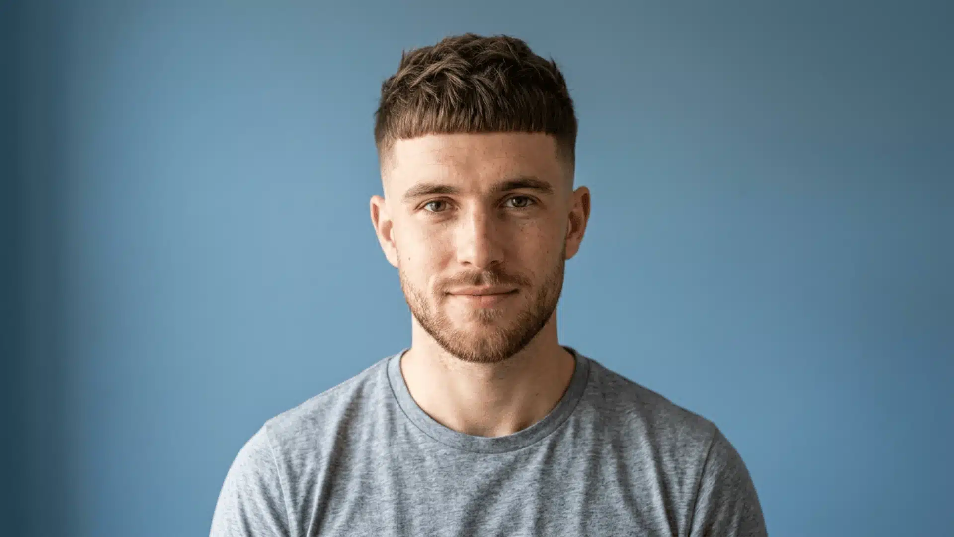 Pale skinned man with a Caesar buzz cut and a short blunt fringe pushed forward