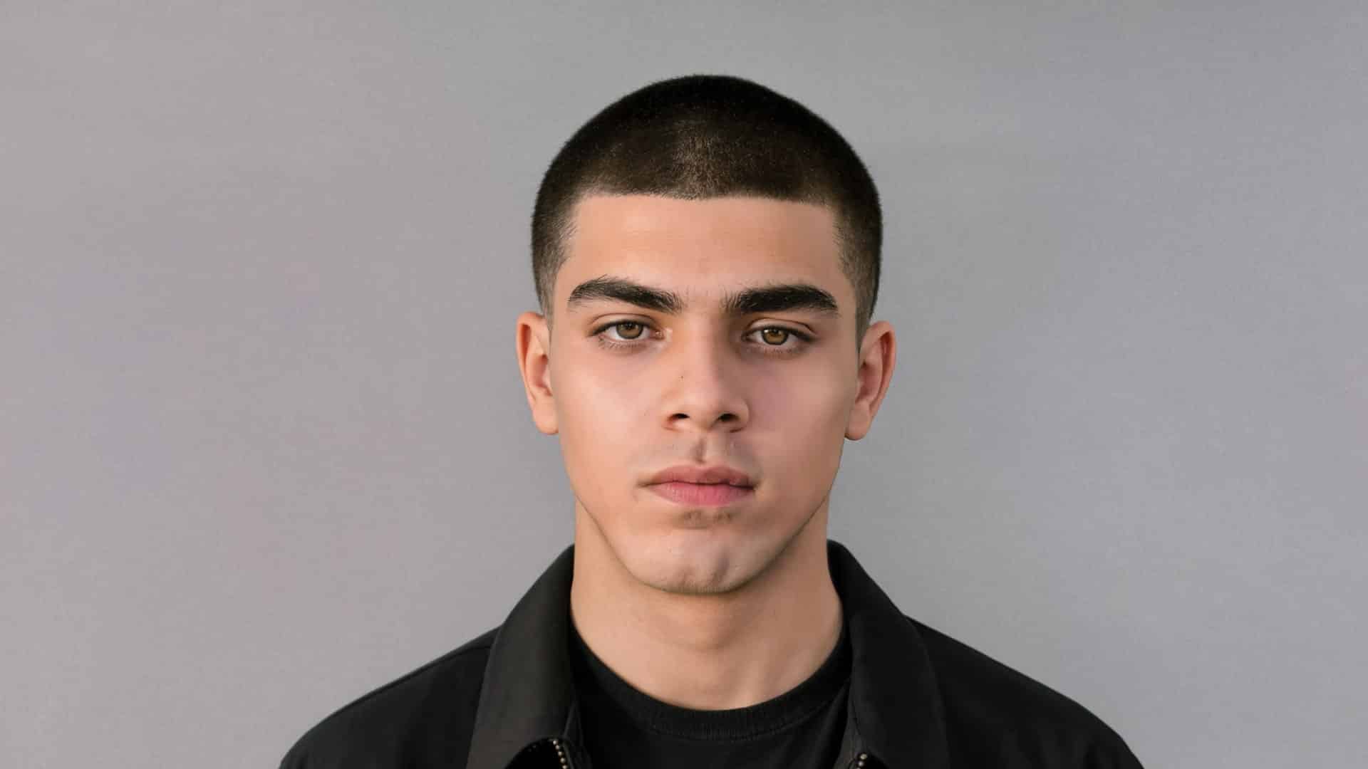 portrait of a young man with a buzz cut Caesar hairstyle, against a solid gray background