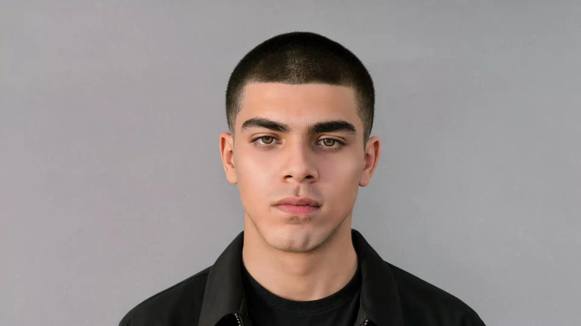 portrait of a young man with a buzz cut Caesar hairstyle, against a solid gray background