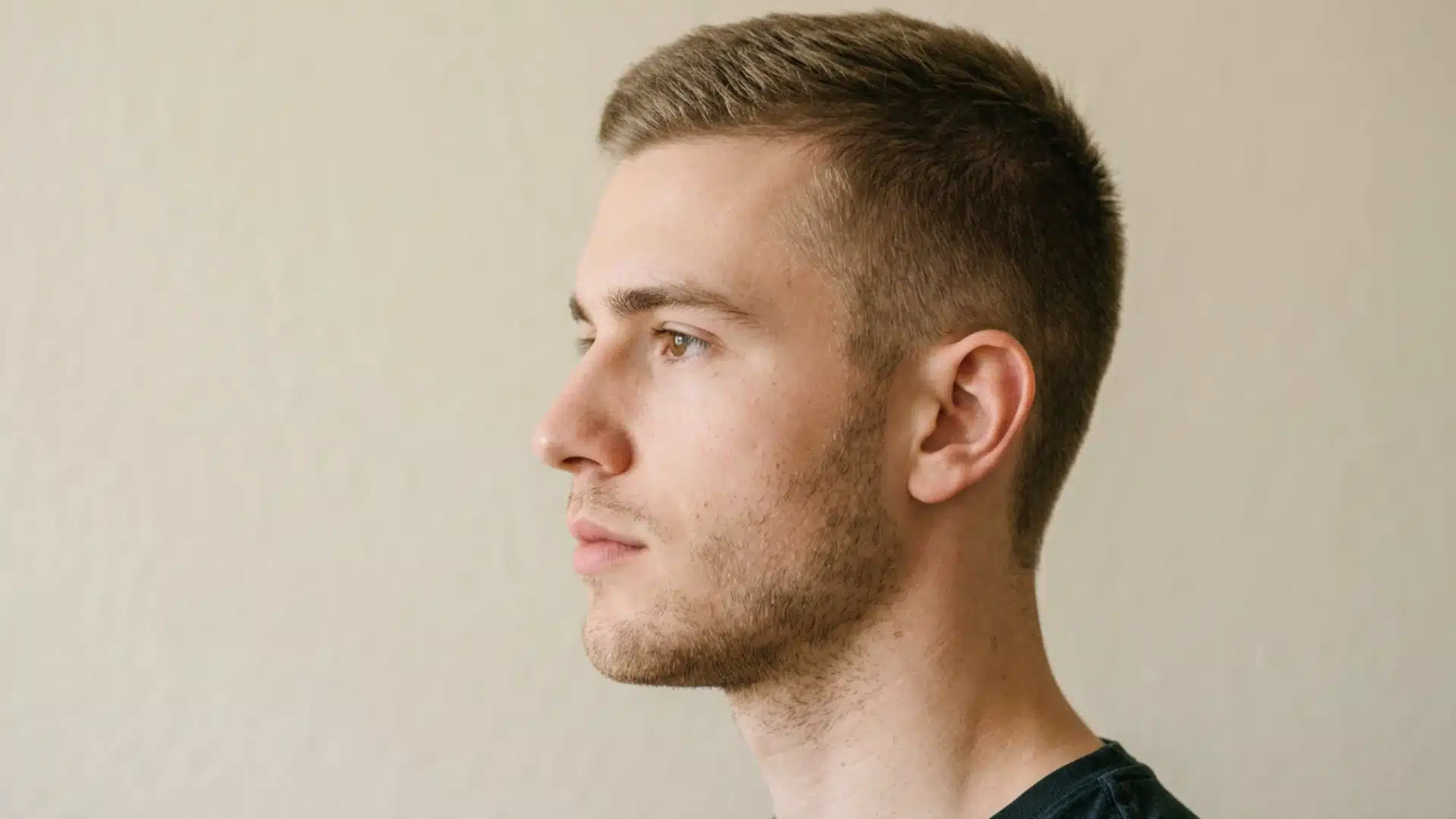 Profile view of a young man showcasing a clean crew cut with faded sides and light facial stubble