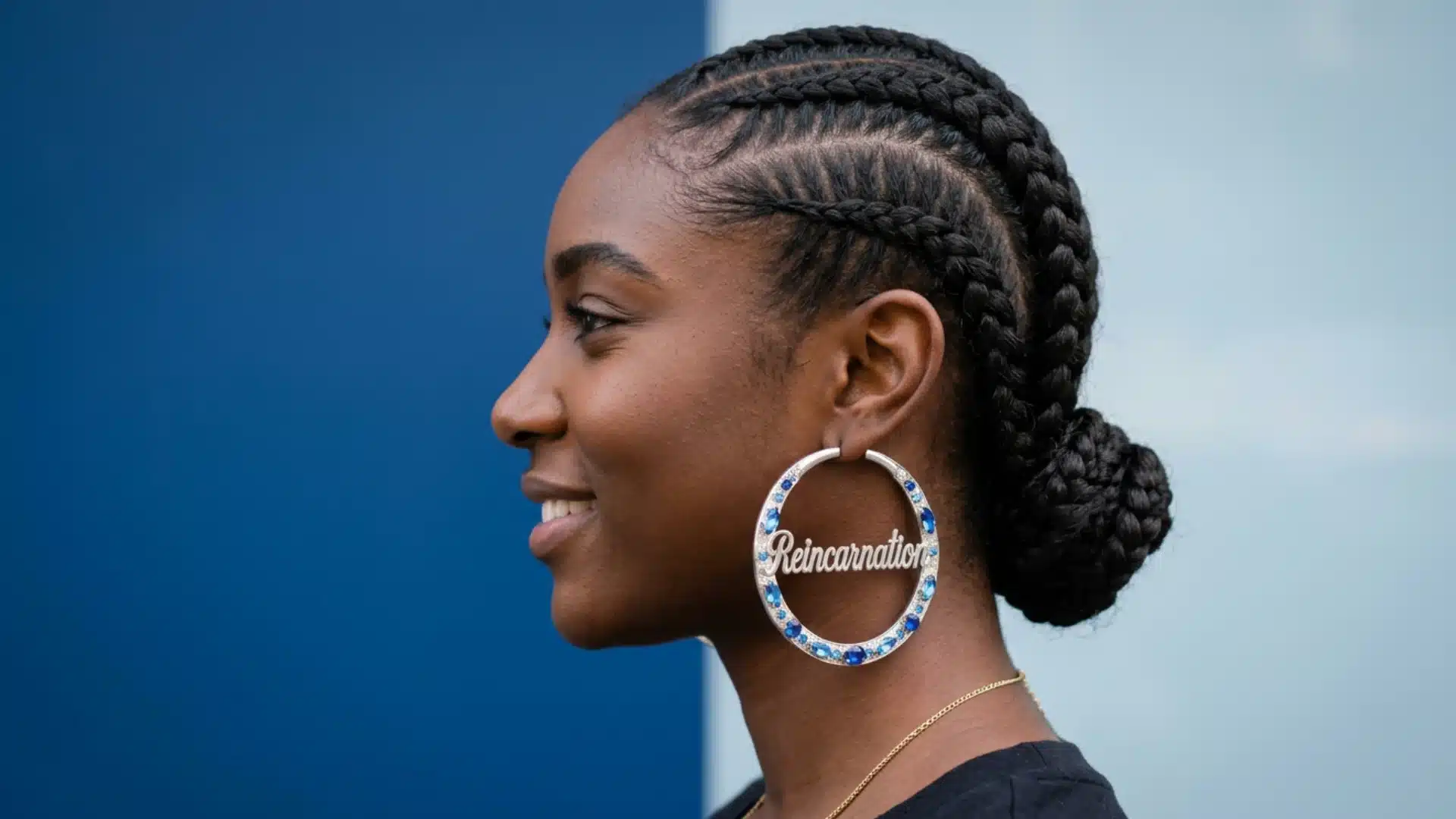 Profile of a smiling Black woman with braided hair wearing large hoop earrings that say Reincarnation