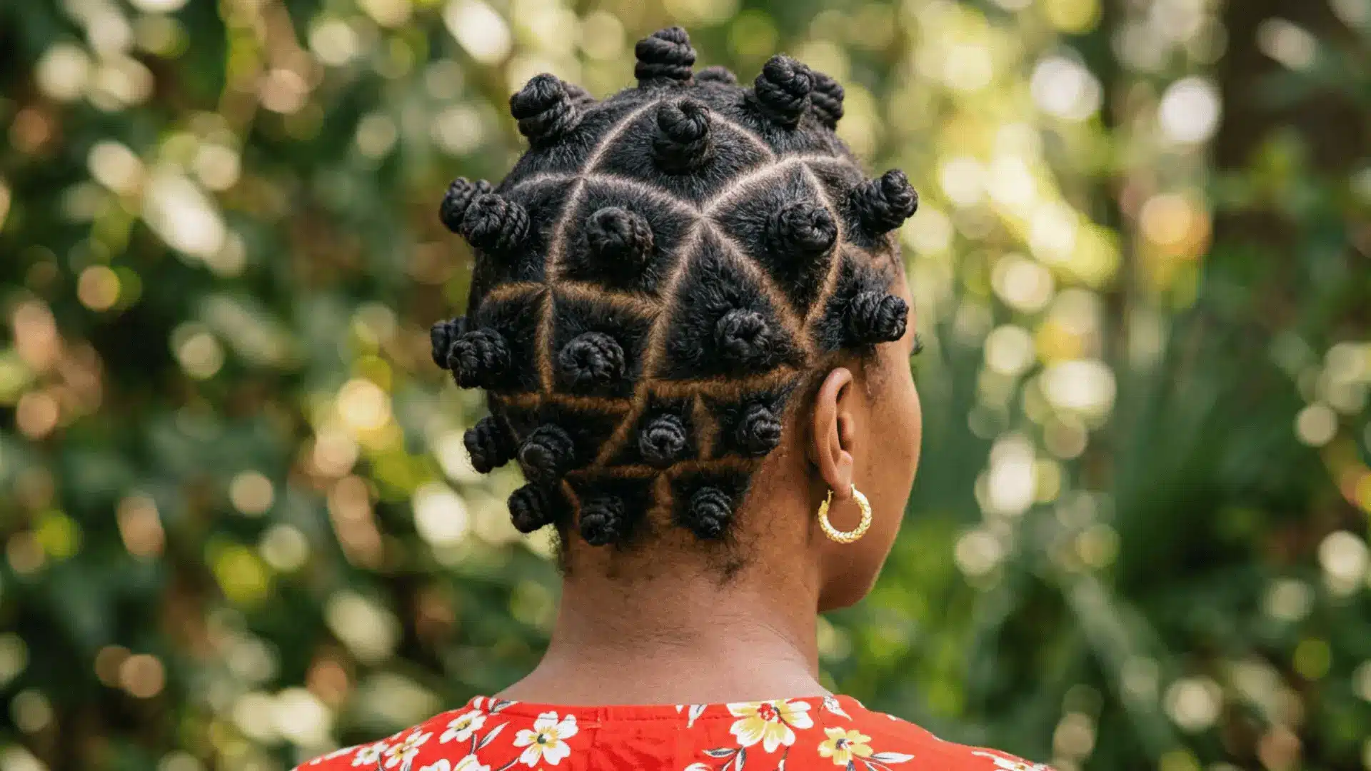 Rear view of a person with dark hair styled into neat Bantu knots with precise triangular parting, outdoors