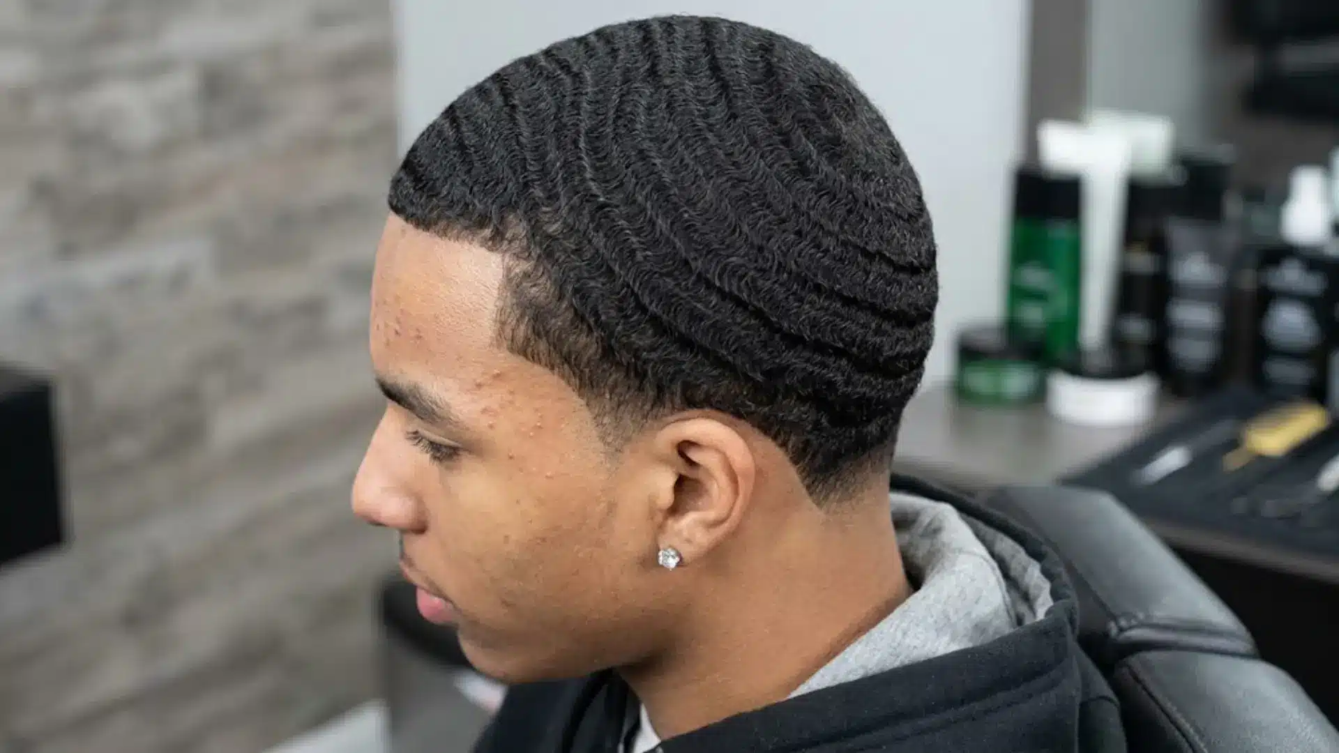 Side profile of a man with 360 waves hairstyle, sharp lineup, and low fade haircut in a barber chair