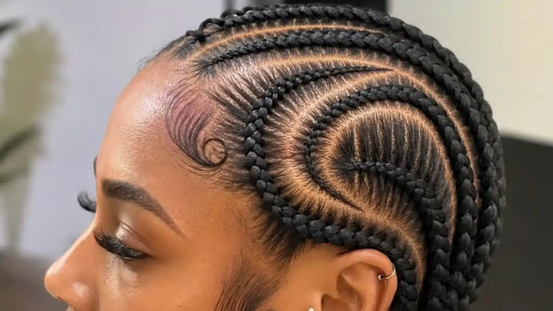 Side profile of a person featuring intricate swirling cornrows, sleek laid edges